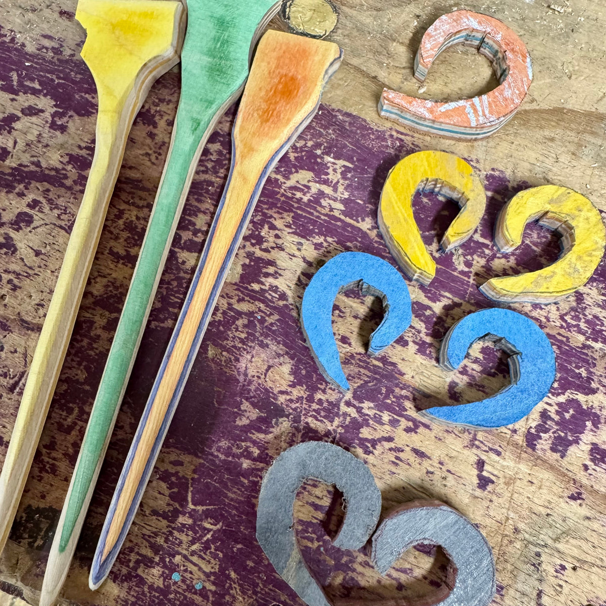 Skateboard maple hair sticks and crescent hair forks in yellow, blue and grey on a purple painted deck.
