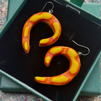 Pair of orange and yellow curved earrings on a black display stand.