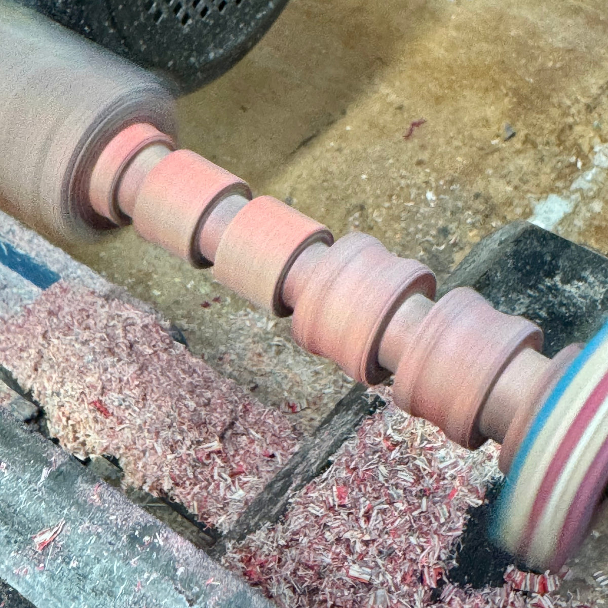Ring blanks mounted on a lathe being turned, with pink wood shavings collected below.