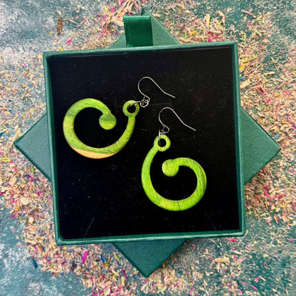 Green spiral earrings in a black box on a textured surface