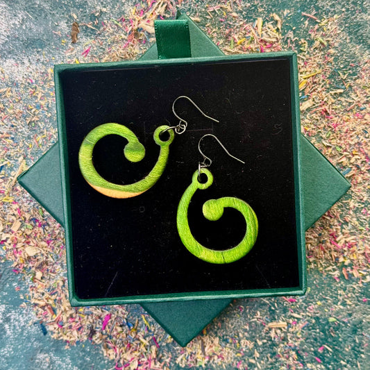 Green spiral earrings in a black box on a textured surface