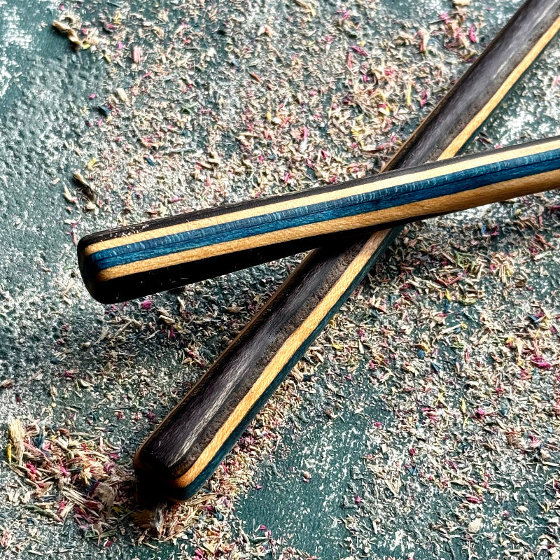 Blue Black Skateboard Hair Sticks made from layered recycled skateboard wood with blue and black accents on textured surface.