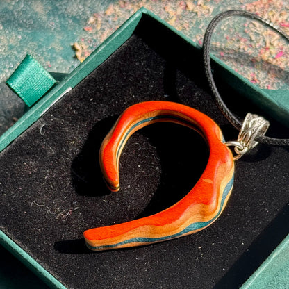 Wooden pendant with a silver chain on a black cushion in a green box.