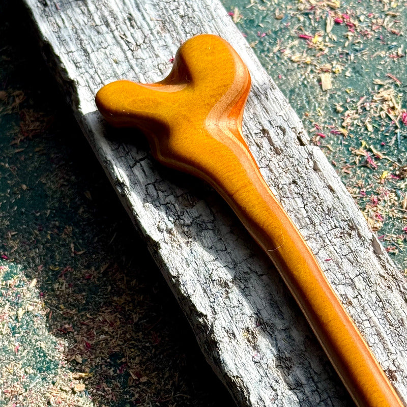 Yellow and Orange Skateboard Hair Stick made from polished wood with smooth curved edges resting on weathered wood surface