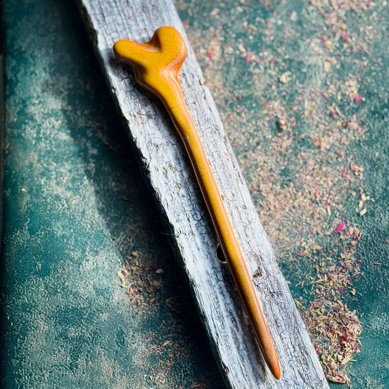 Yellow and Orange Skateboard Hair Stick made from smooth polished wood with a sculpted top shape placed on a textured surface