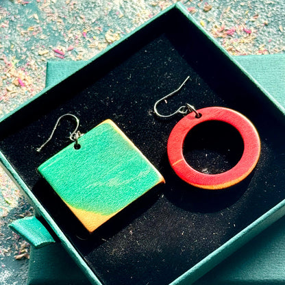 Two pairs of earrings, one green square and one red circle, in a green box.