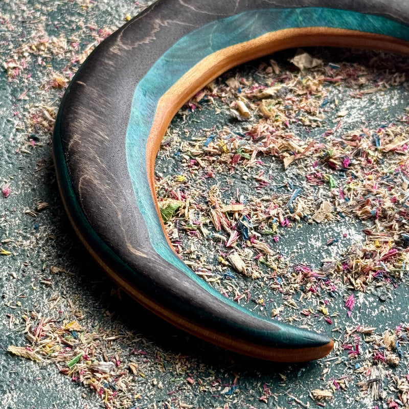 Close-up of a crescent moon hair fork showing black, teal and orange skateboard maple layers.
