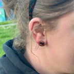Small round wooden stud earring shown on the ear for scale.