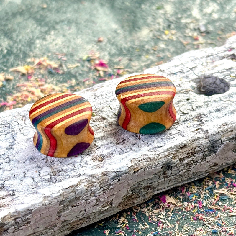 Recycled skateboard wood plugs in multicolour tones with green and purple circular accents, displayed on a weathered wooden surface.