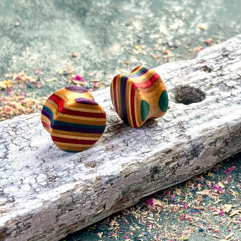 Multicolour wooden plugs handcrafted from recycled skateboard wood, featuring curved shape and teal accent dots, photographed on a weathered wooden surface.