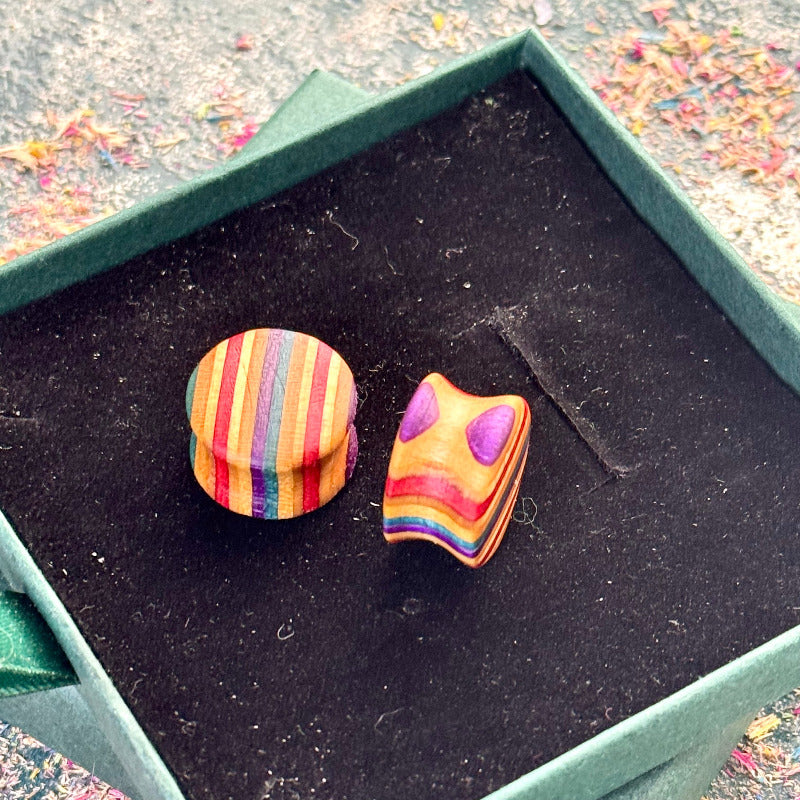 Hand-shaped wooden plugs made from recycled skateboard wood, showing bright striped colour tones in purple, red, orange and natural maple, photographed inside a green jewellery box.