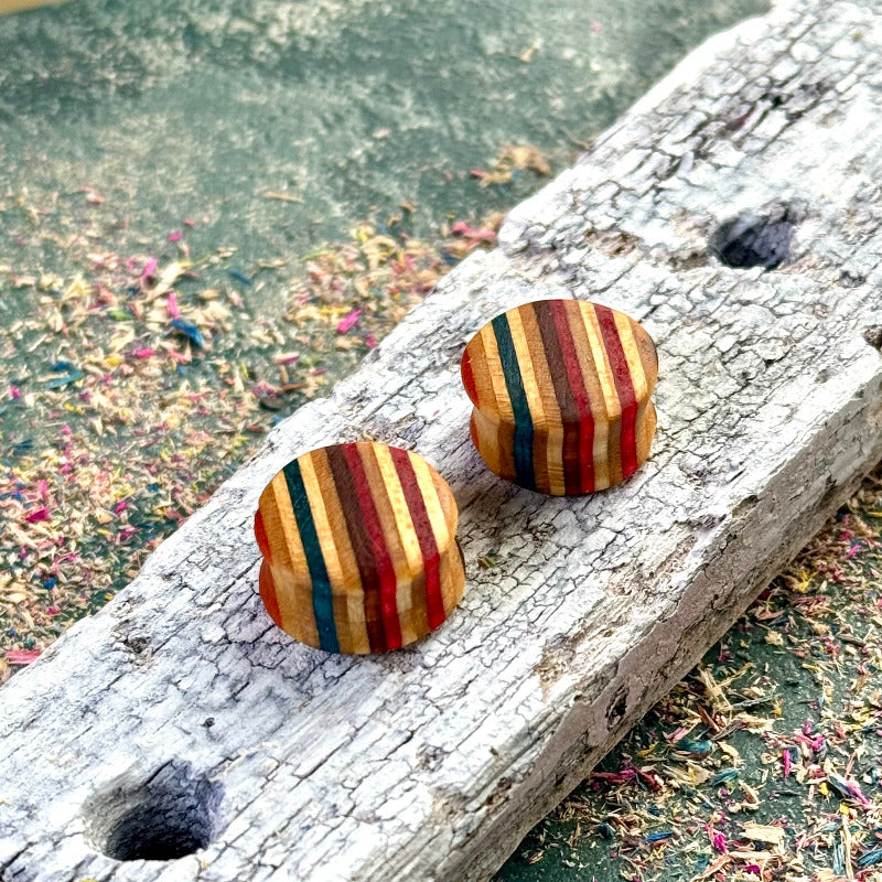 Handmade wooden ear plugs from recycled skateboard wood with red, blue and yellow colour tones, shown on a textured wooden surface for detail.