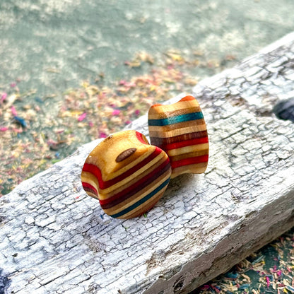 Handmade recycled-skateboard wood plugs with curved shape, showing red, yellow and blue colour tones on a weathered wooden surface.