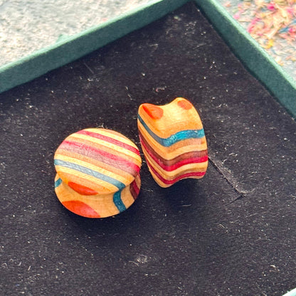 Multicolour wooden ear plugs handmade from recycled skateboard wood, featuring teal, red, yellow and blue colour tones on a black background.