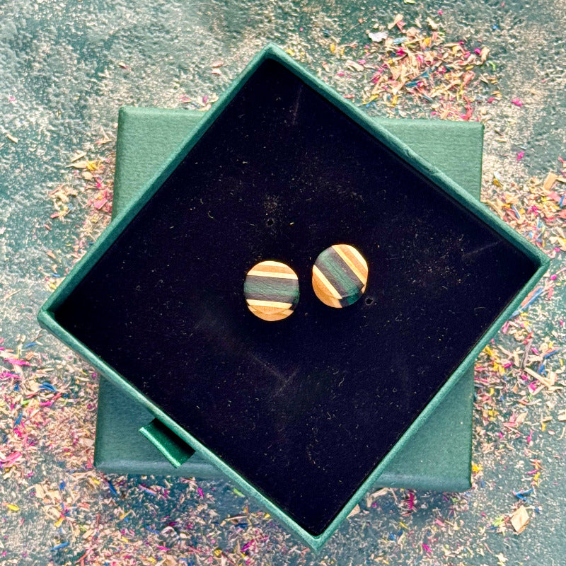 Pair of handcrafted wooden ear plugs made from recycled skateboard wood, shown inside a dark velvet jewellery box.