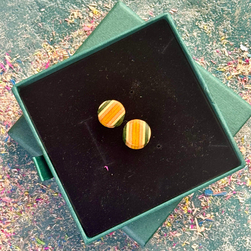 Small round wooden plugs made from recycled skateboard wood in green, yellow and orange colour tones, shown in a dark velvet box.
