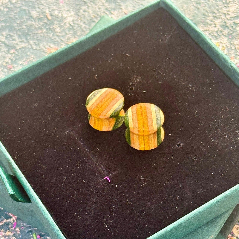 Handmade wooden ear plugs made from recycled skateboard wood with natural and green colour tones, shown close-up on a dark display pad.