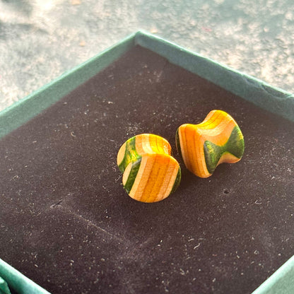 Handmade wooden plugs from recycled skateboard wood with green and yellow colour tones, shown resting in a dark-lined gift box.