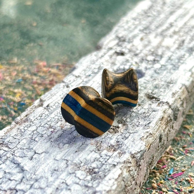 Handmade skateboard wood plugs with blue and black colour tones displayed on a textured wooden surface.