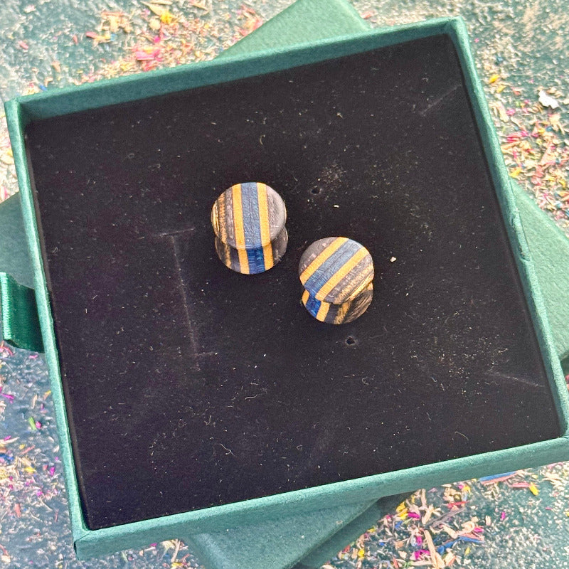 Handmade wooden plugs made from recycled skateboard wood with blue and black colour tones, photographed on a black display box.