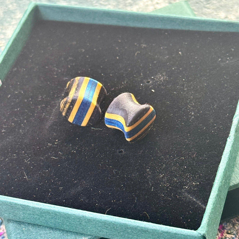 Handmade recycled skateboard plugs in blue and black tones displayed on a dark jewellery box.