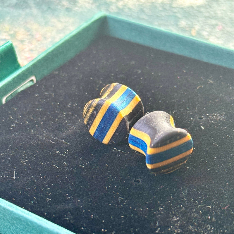 Handmade recycled skateboard wood plugs with blue and black colour tones, displayed in a jewellery box on a textured background.
