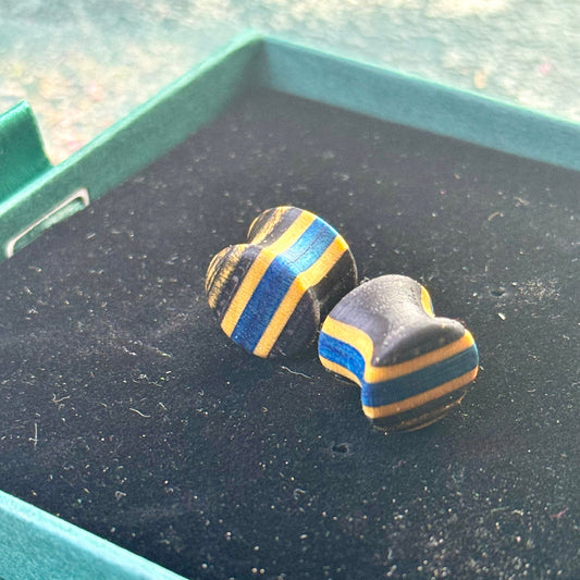 Handmade recycled skateboard wood plugs with blue and black colour tones, displayed in a jewellery box on a textured background.
