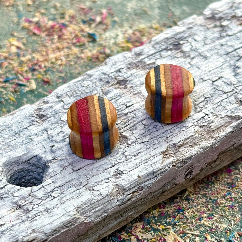 Handmade recycled skateboard wood plugs with vertical red, blue and natural colour tones displayed on weathered wood.