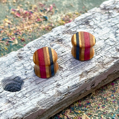 Handmade recycled skateboard wood plugs with vertical red, blue and natural colour tones displayed on weathered wood.