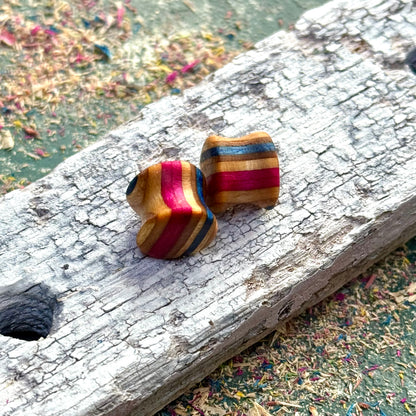 Recycled skateboard wood plugs with red and blue colour tones displayed on a textured wooden block.
