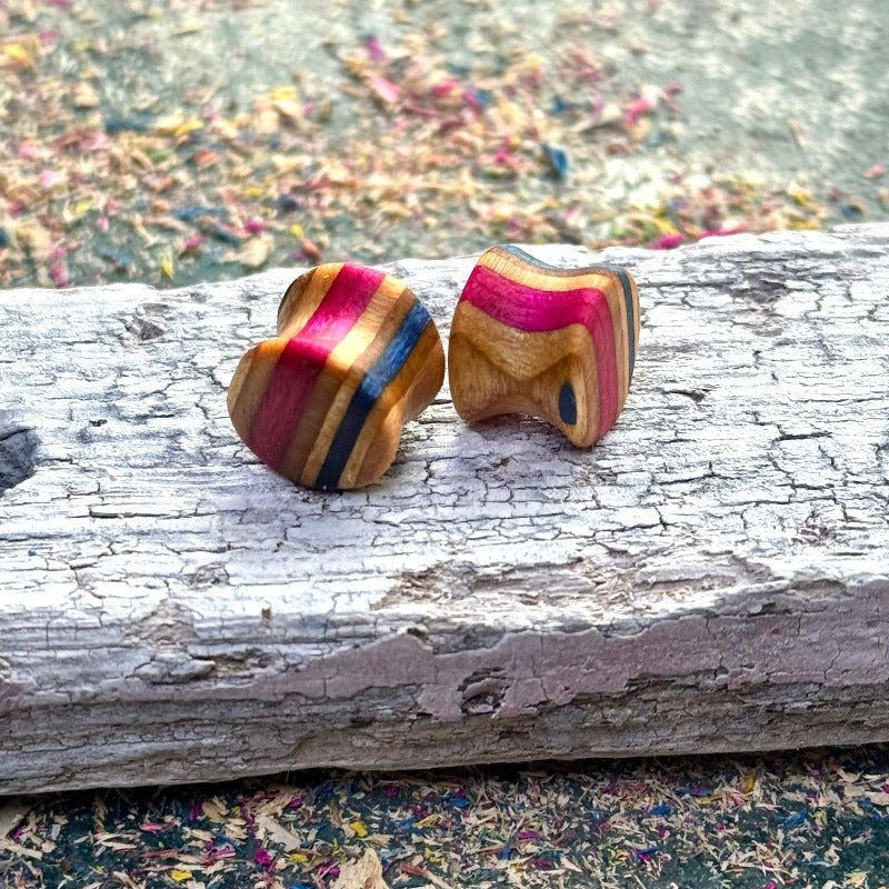 Handmade skateboard wood plugs with red, blue and natural colour tones displayed on a textured wooden surface.