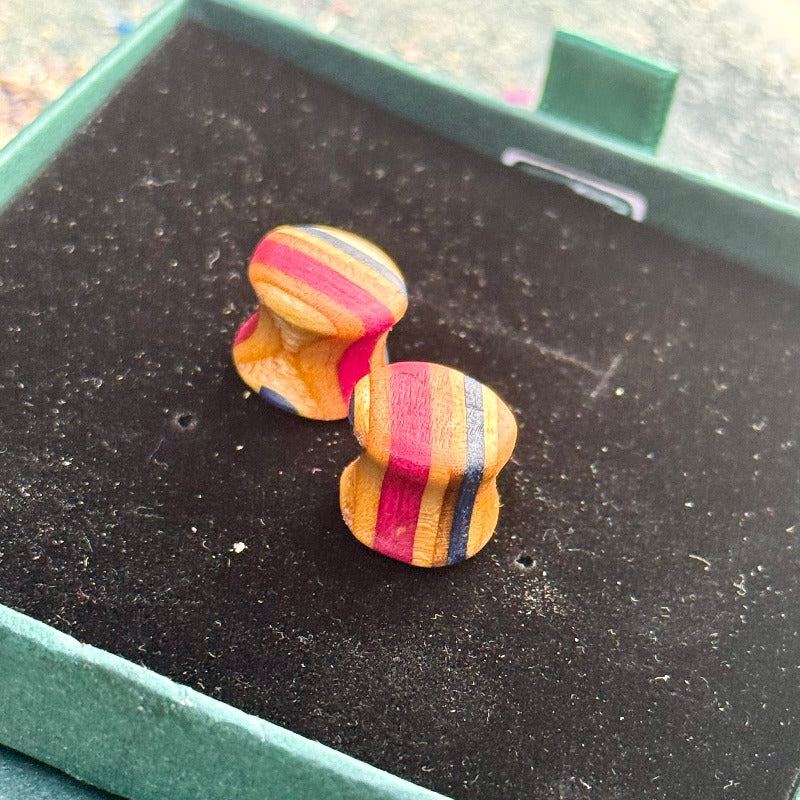 Handmade recycled skateboard wood plugs in red, purple and natural tones, shaped with a curved profile and shown on a black velvet box.