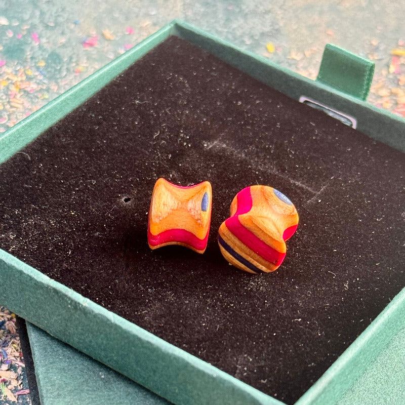 Handmade recycled skateboard wood plugs with curved shape showing red, natural wood and blue colour tones, displayed in a green gift box.