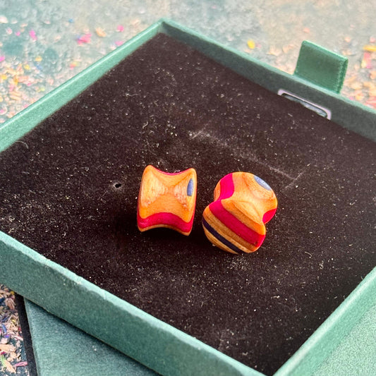 Handmade recycled skateboard wood plugs with curved shape showing red, natural wood and blue colour tones, displayed in a green gift box.