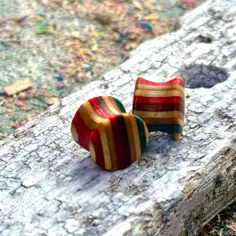 Handmade skateboard wood plugs with red, teal and natural colour tones displayed on weathered bark.