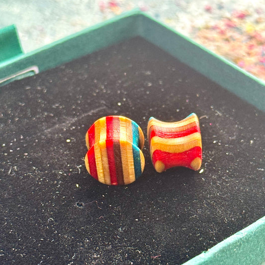 Handmade recycled skateboard wood plugs in red, blue and natural wood colour tones displayed in a green jewellery box.