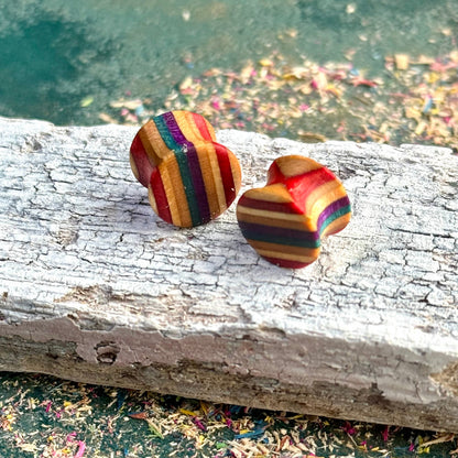 Recycled skateboard wood plugs with curved shape in purple, red and teal colour tones, shown on a weathered white wooden surface.