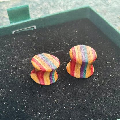 Handmade recycled skateboard wood plugs with curved profile, showing multicoloured red, purple, teal and yellow colour tones on a black backdrop.