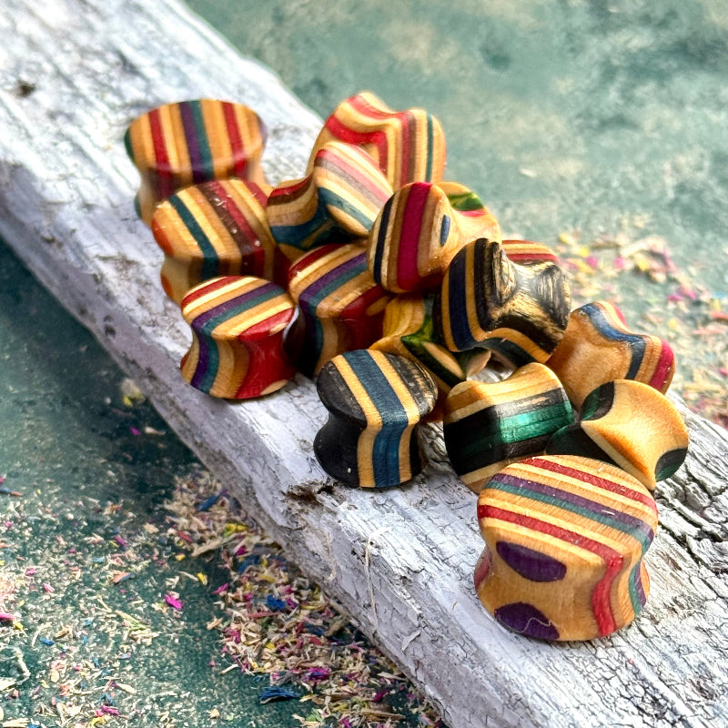 Custom Double Flare Ear Plugs and Tunnels made from layered wood with colorful striped patterns on a textured surface
