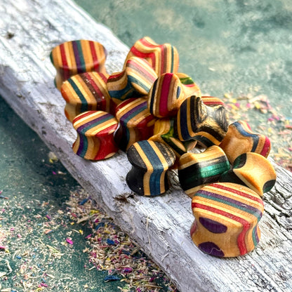 Custom Double Flare Ear Plugs and Tunnels made from layered wood with colorful striped patterns on a textured surface