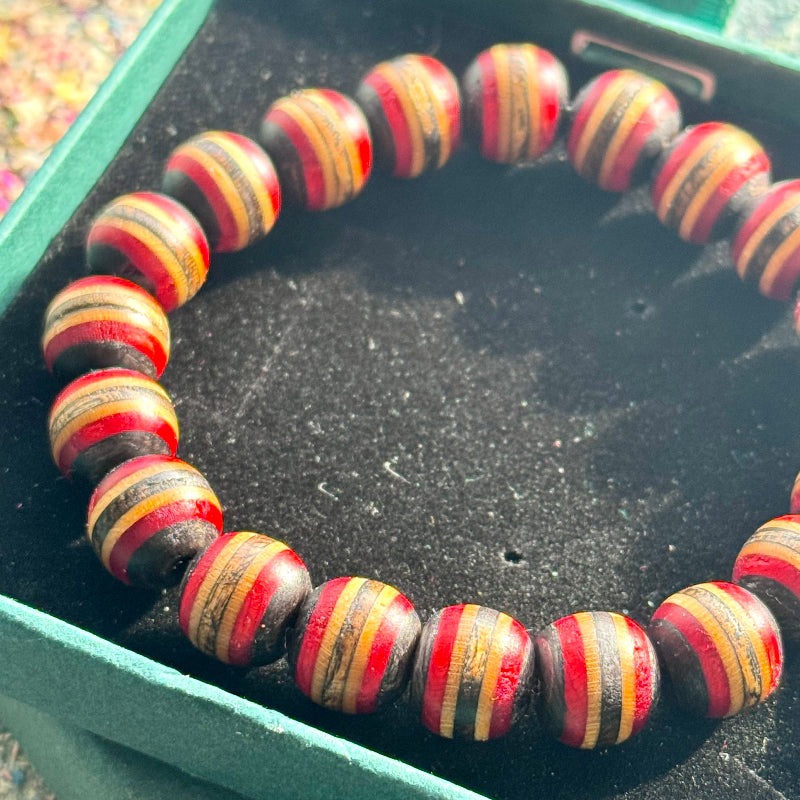 Beaded bracelet made from recycled skateboard wood with red, black and yellow colour tones displayed in a green gift box.