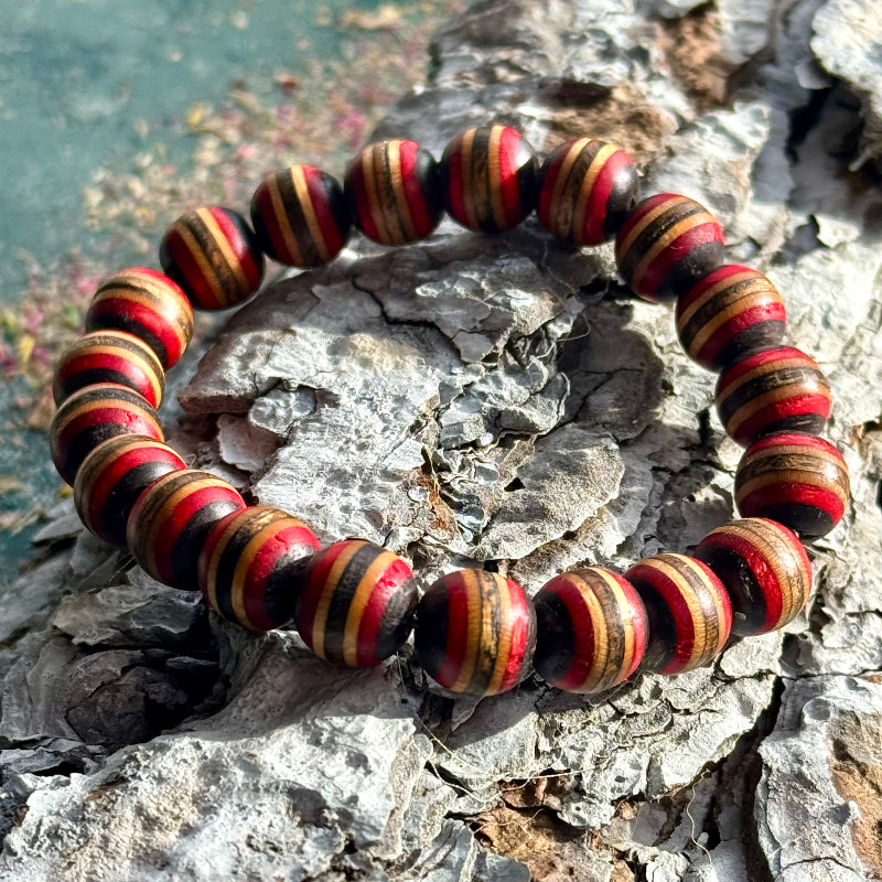 Red, black and natural skateboard wood bracelet photographed on textured bark.