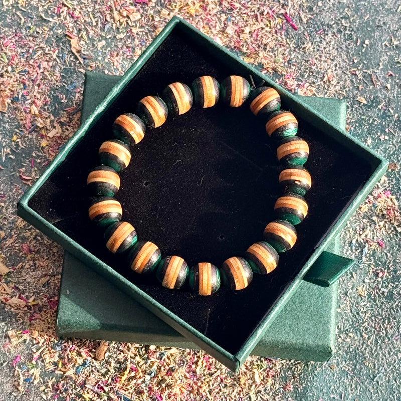 Teal and black skateboard wood bead bracelet resting on the lid of its green gift box outdoors.