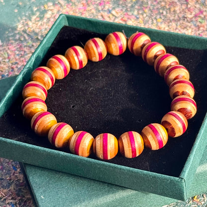 Bracelet made from recycled skateboard wood, shown in a gift box with warm yellow and pink bead tones on a dark insert.