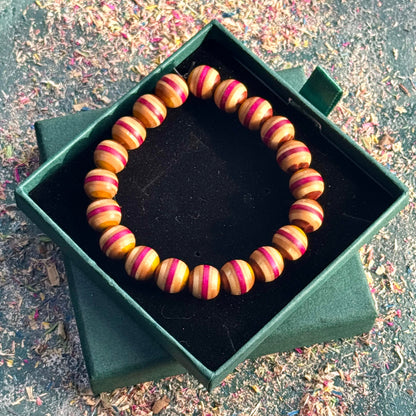 Close-up of a beaded skateboard wood bracelet in red and yellow tones, displayed on a dark gift box with scattered workspace shavings.
