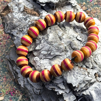 Beaded bracelet made from recycled skateboard wood in warm yellow and deep pink tones, shown on textured bark background.