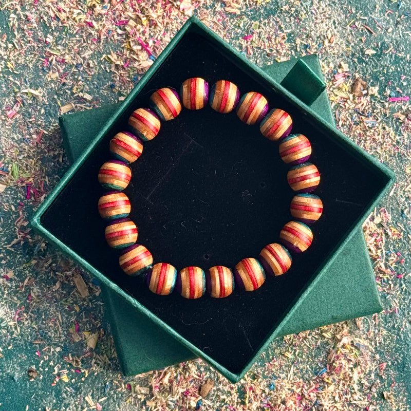 Teal, red and purple skateboard-wood bead bracelet displayed in a green gift box, photographed from above on a textured background.