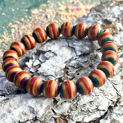 Teal, red and purple skateboard-wood bead bracelet shown on textured bark background.