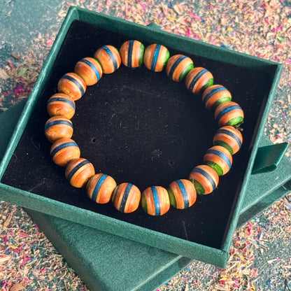Close-up of a recycled skateboard wood bracelet showing blue and green tones on rounded beads, photographed in an open gift box.