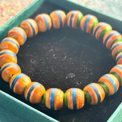 Handmade beaded bracelet crafted from recycled skateboard wood, featuring alternating orange, blue and green colour tones on rounded beads, displayed on a dark jewellery box.
